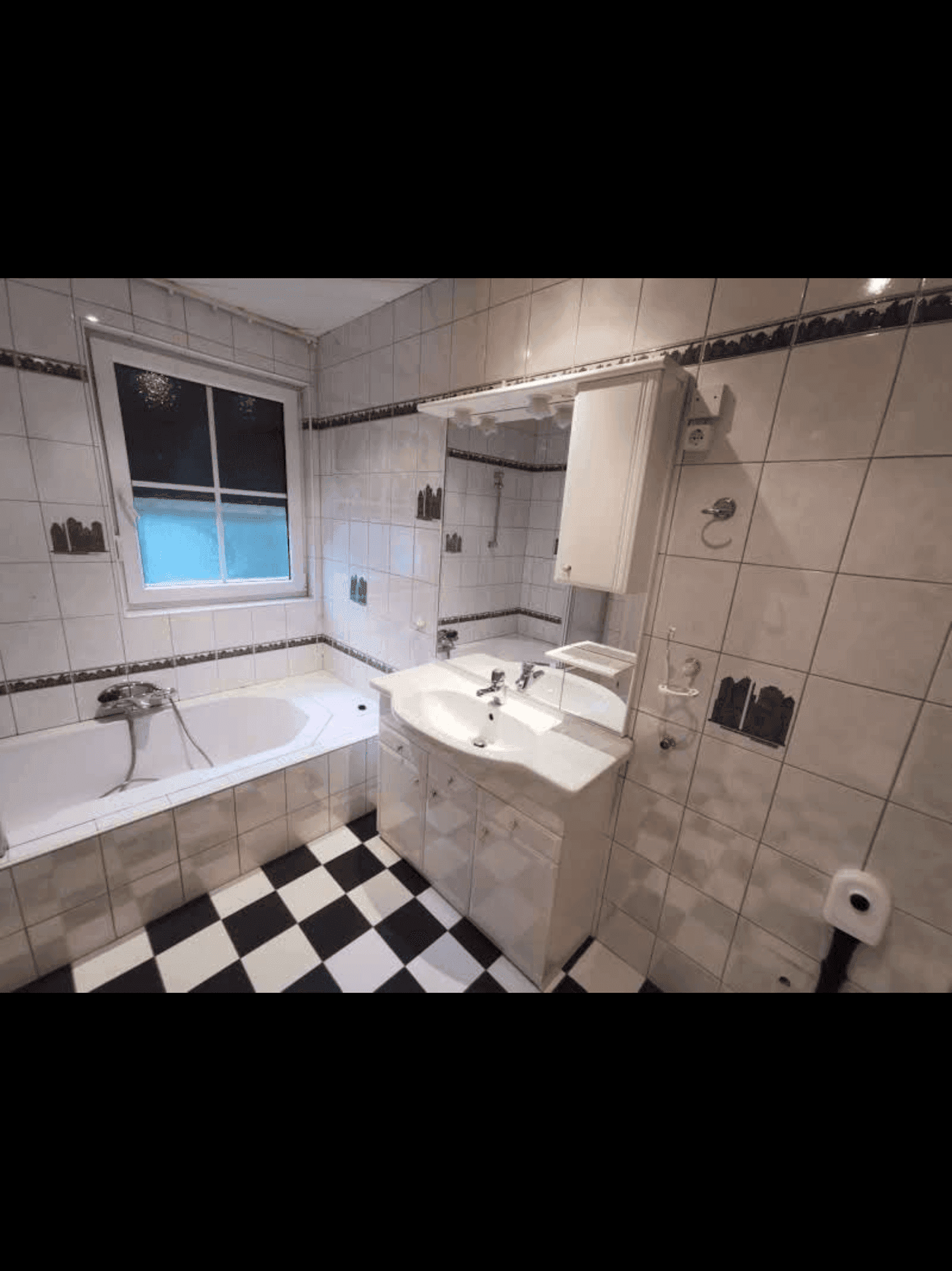 Badezimmer mit Badewanne, Waschbecken und markantem schwarz-weiß kariertem Fliesenboden.