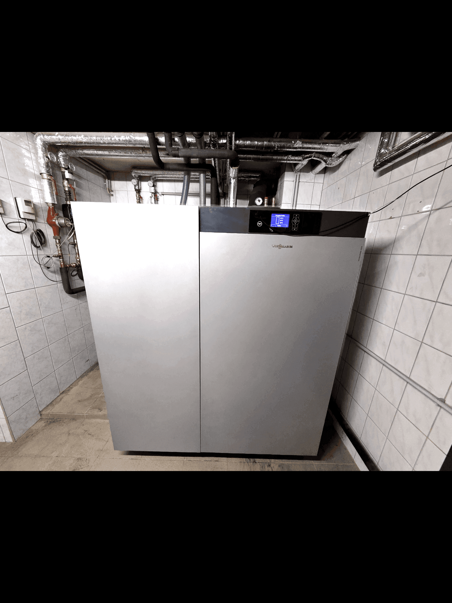 Heizungsraum mit einer modernen Viessmann-Heizanlage und sichtbaren Rohrleitungen an gefliesten Wänden.