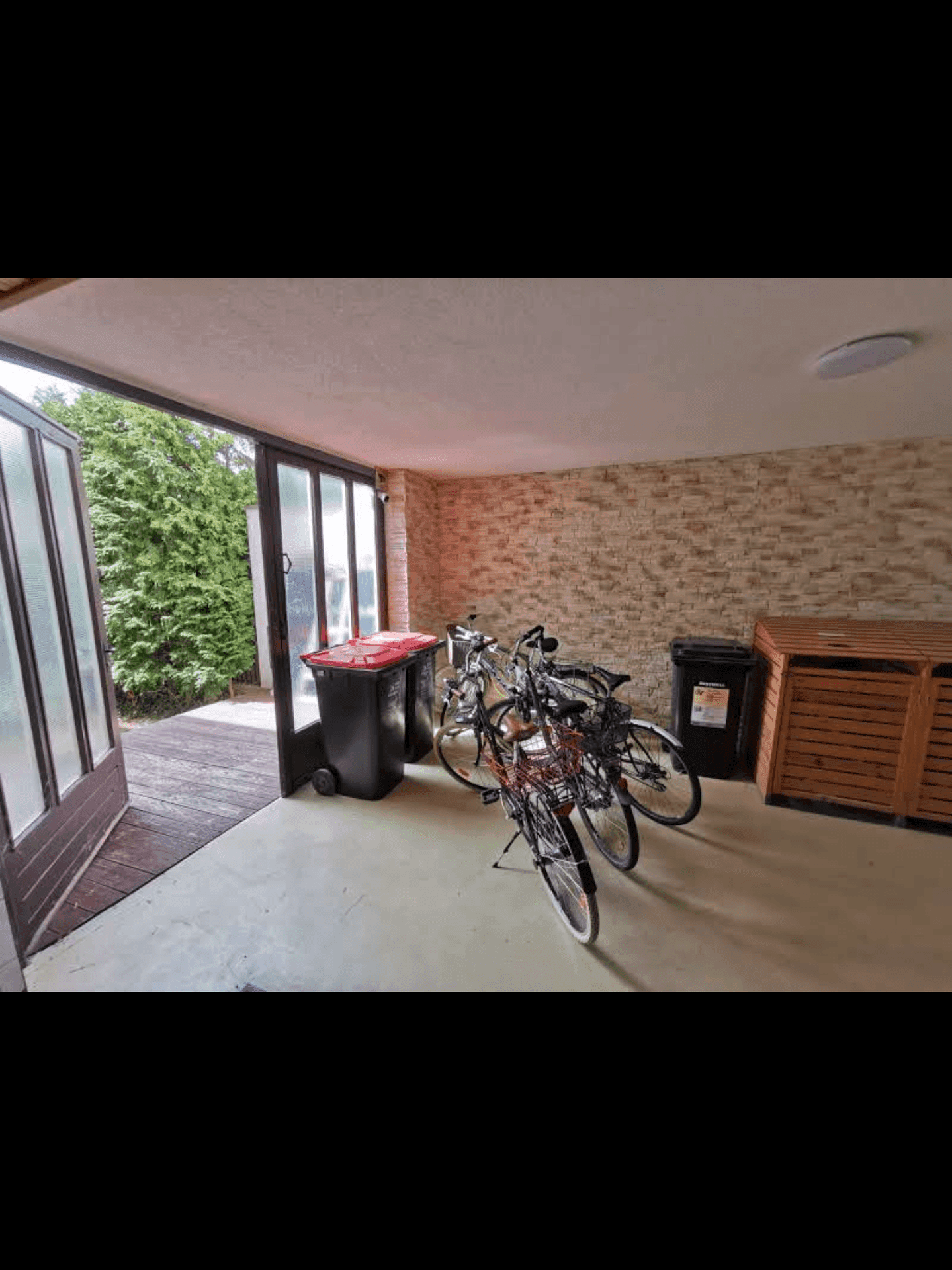 Überdachter Bereich mit Fahrrädern und Mülltonnen, mit Zugang zum Garten.