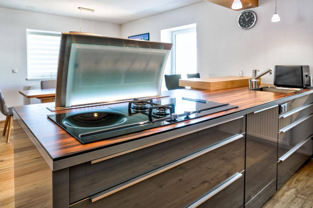 Moderne Küche mit Kochinsel, integriertem Gaskochfeld, ausfahrbarer Dunstabzugshaube und glänzenden Schränken.