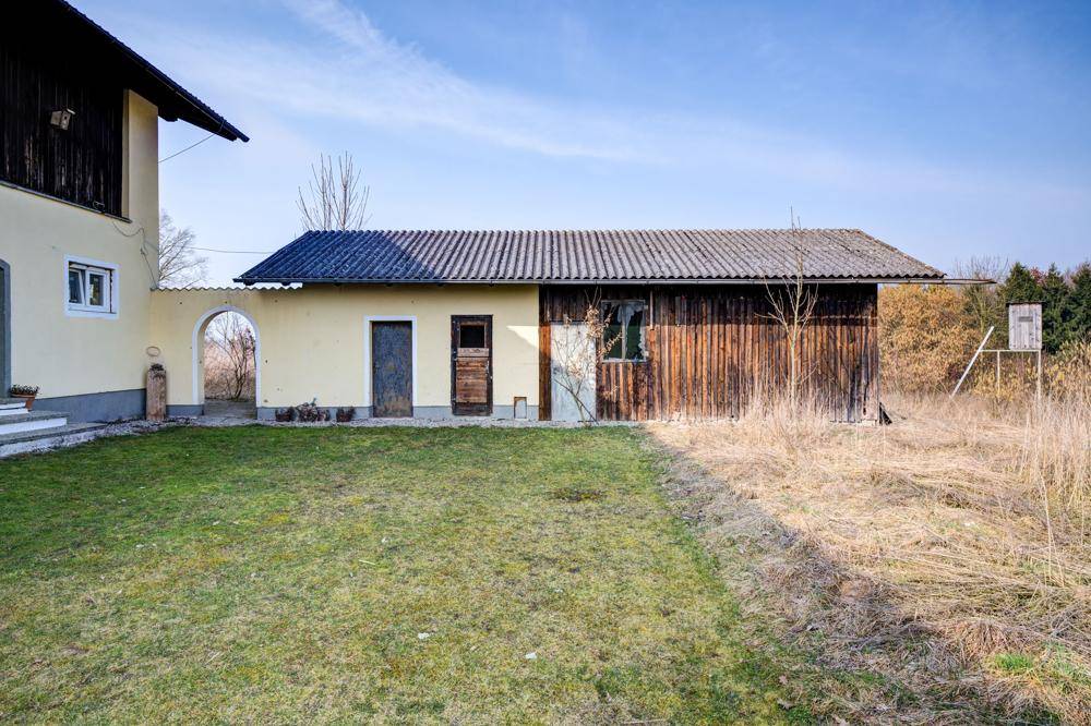 Nebengebäude mit Holzwänden und Wellblechdach neben dem Haupthaus und Rasenfläche.