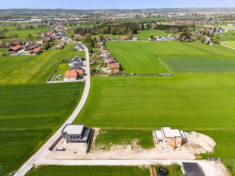 Weitläufige Luftaufnahme von zwei Neubauten in einer ländlichen Siedlung mit weiten Grünflächen.