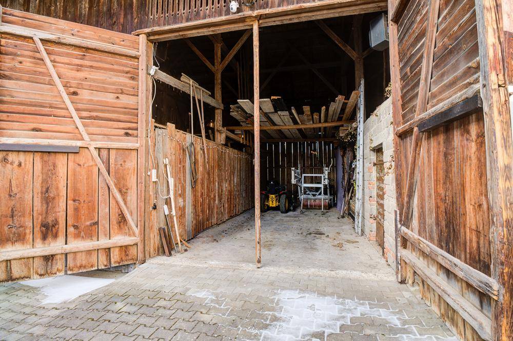 Offene Scheune mit Holzbalken und Lagerflächen, die landwirtschaftliche Geräte beherbergt.