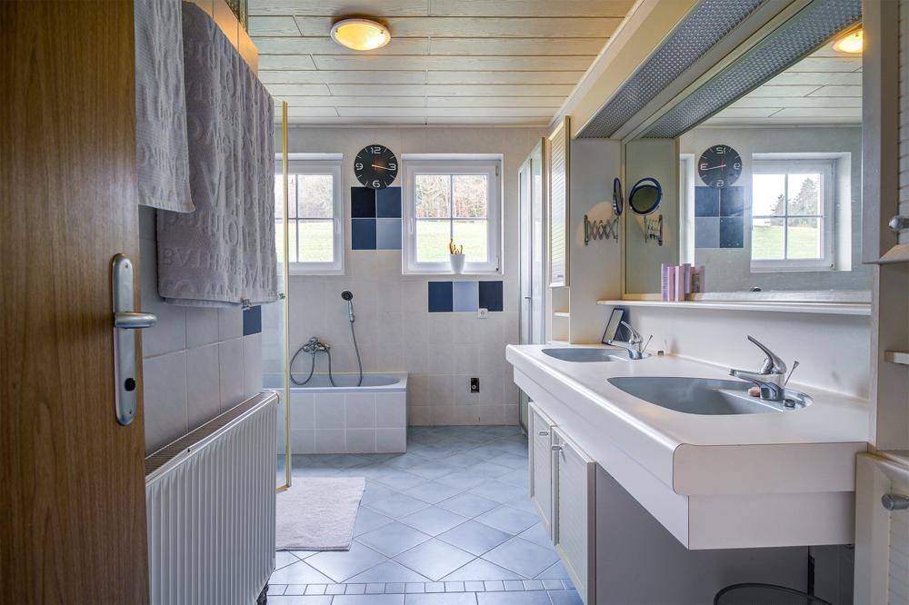 Badezimmer mit Doppelwaschbecken, Badewanne und Fenstern mit Blick auf die Landschaft.