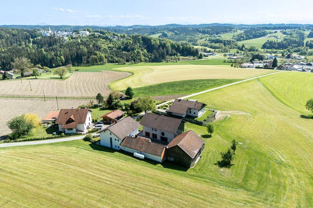 Weitläufige Luftaufnahme einer ländlichen Siedlung mit Häusern und Feldern unter blauem Himmel.