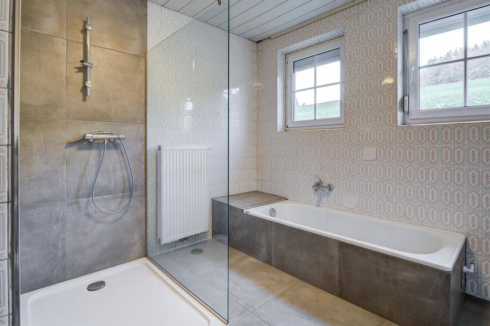 Modernisiertes Badezimmer mit Badewanne, begehbarer Dusche und zwei Fenstern.
