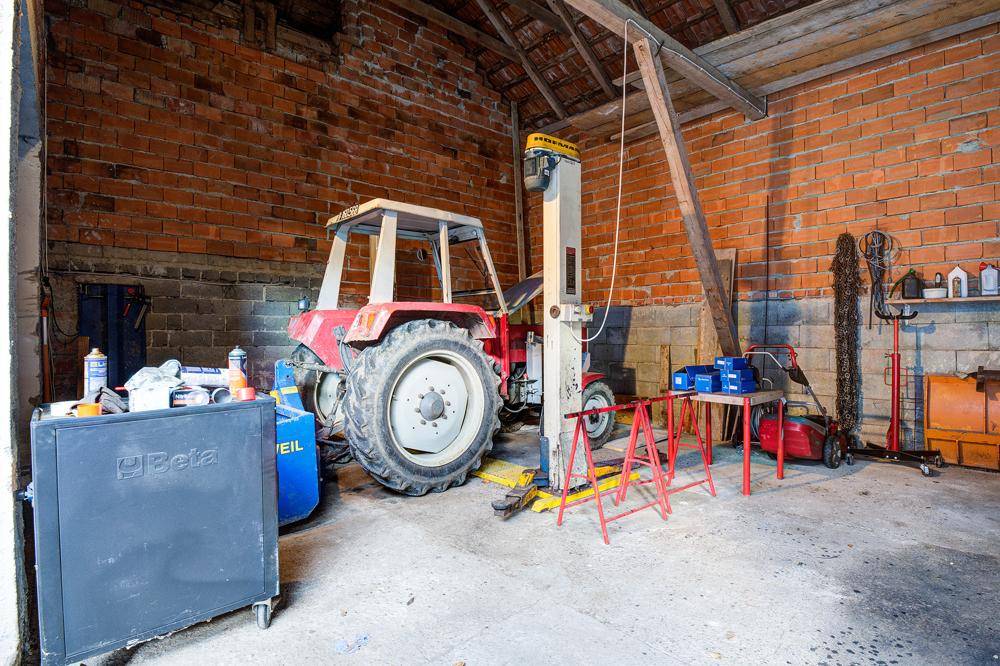 Werkstatt mit Traktor, Hebebühne und Ziegelwänden, bereit für Reparaturen.