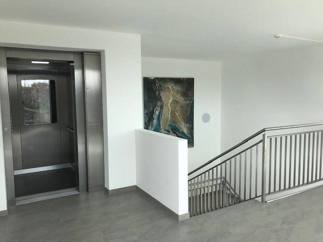 Heller Treppenhausbereich mit modernem Aufzug und Kunstwerk an der Wand.