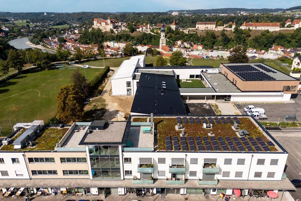 Weitläufige Luftaufnahme einer Stadt mit Fluss, Grünflächen und modernem Gebäudekomplex.