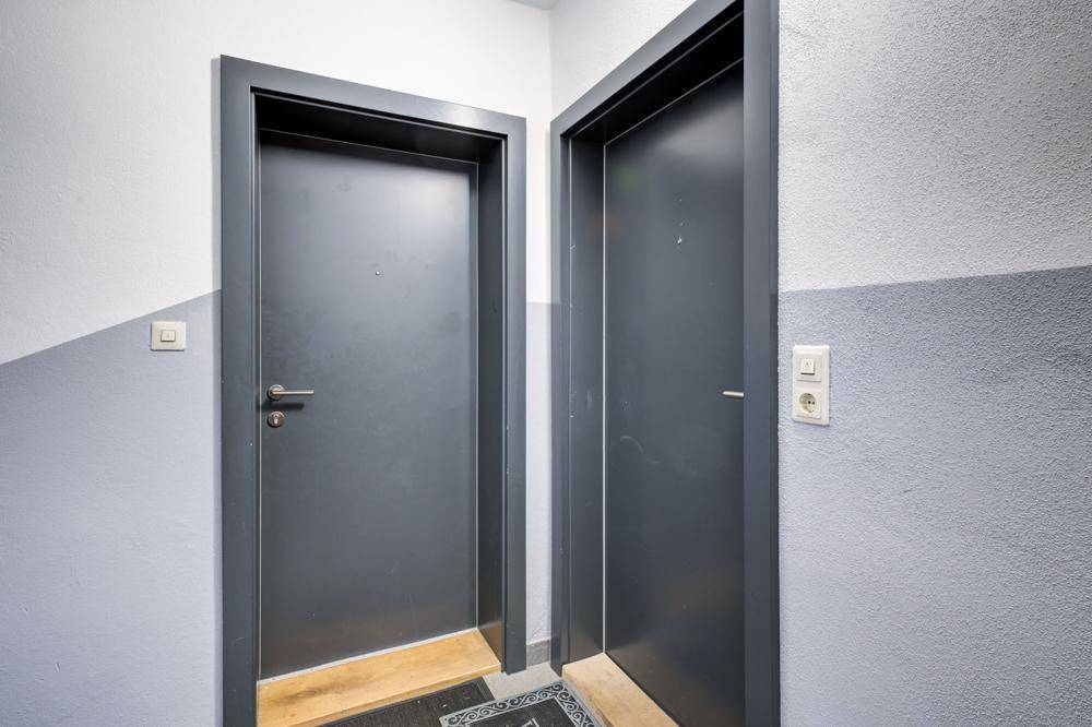 Zwei Wohnungseingangstüren in einem Flur mit grauen Wänden und dunklen Türrahmen.