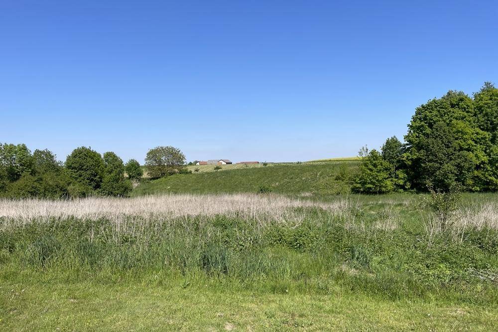 Panoramablick über weite Felder und sanfte Hügel mit vereinzelten Gebäuden in der Ferne.