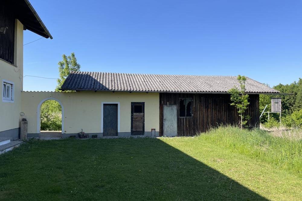 Nebengebäude mit Holzwänden und Wellblechdach neben dem Haupthaus mit Torbogen.