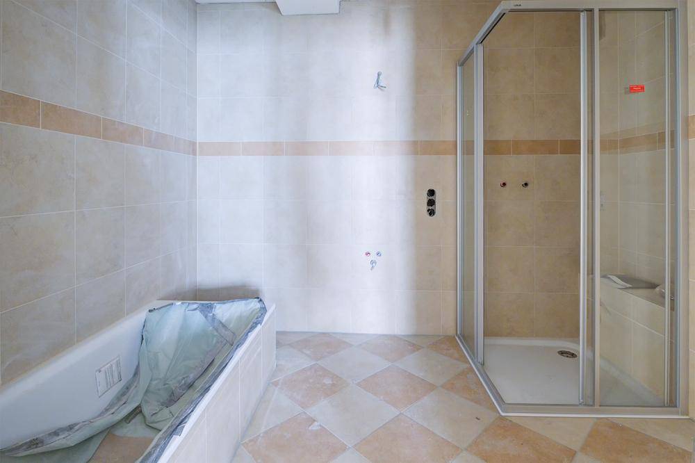 Badezimmer im Renovierungszustand mit beigefarbenen Fliesen, Badewanne und Duschkabine.