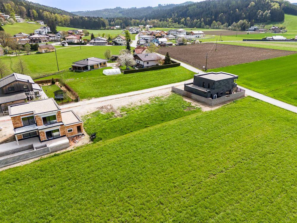 Panoramablick aus der Luft auf zwei moderne Häuser in Bauphase, eingebettet in eine grüne Landschaft.