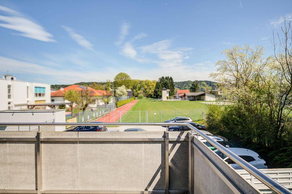 Blick vom Balkon auf einen Sportplatz und die grüne Hügellandschaft in der Ferne.