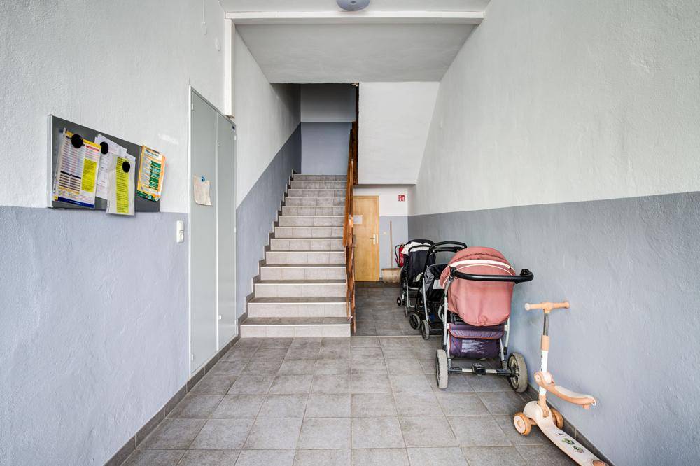 Gemeinschaftlicher Eingangsbereich mit Treppenaufgang, Fliesenboden und Abstellmöglichkeiten für Kinderwagen.