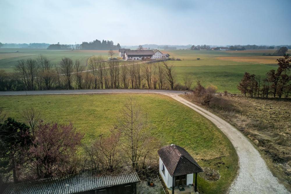 Luftaufnahme einer kleinen Kapelle und eines Feldwegs, umgeben von grünen Feldern.