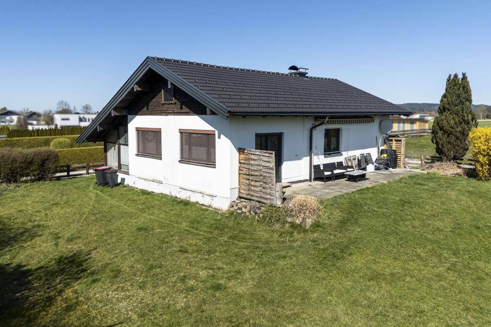 Rückansicht des Hauses mit Rasenfläche, kleiner Terrasse und Gartenmöbeln.