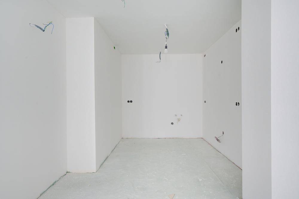 Leerer Raum im Rohbau mit weißen Wänden und sichtbaren Elektroinstallationen.