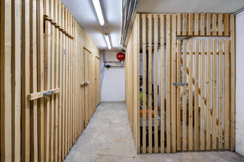 Kellerabteile mit Holzlattenwänden und Betonboden, ideal für zusätzlichen Stauraum im Untergeschoss.