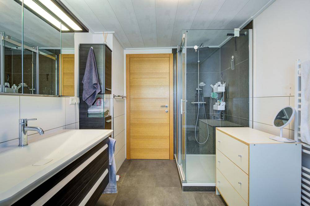 Helles Badezimmer mit moderner Duschkabine, Waschbecken und beheiztem Handtuchhalter.