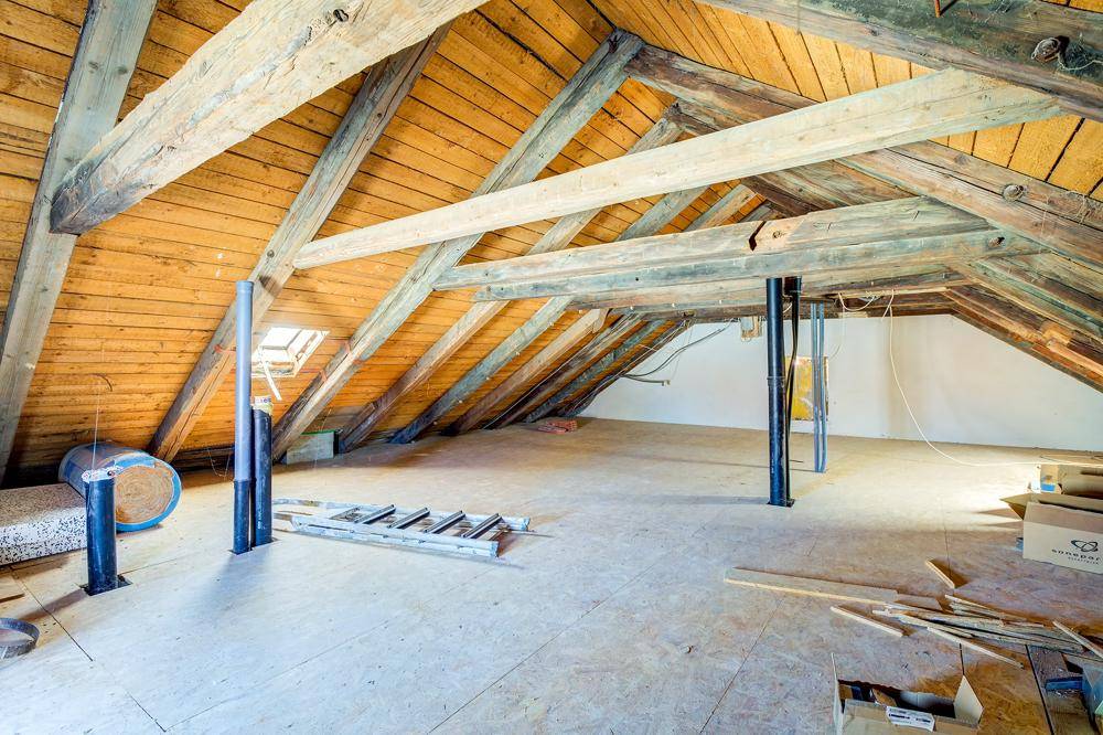 Geräumiger Dachboden mit sichtbaren Holzbalken, Dachschrägen und einem Dachfenster.