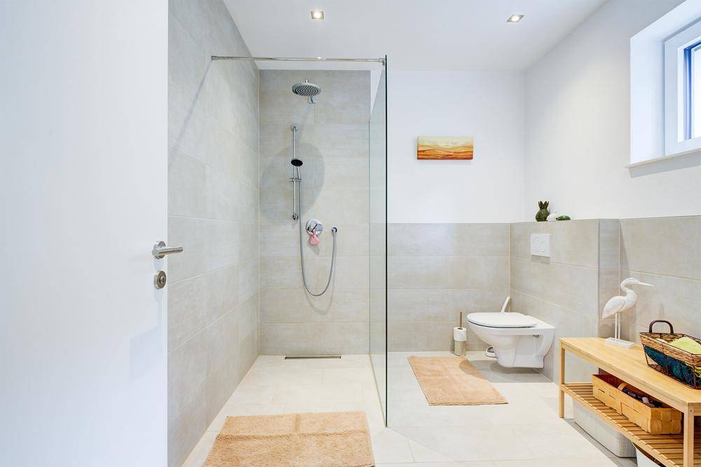 Modernes Badezimmer mit begehbarer Dusche, Wand-WC und hellen Fliesen.