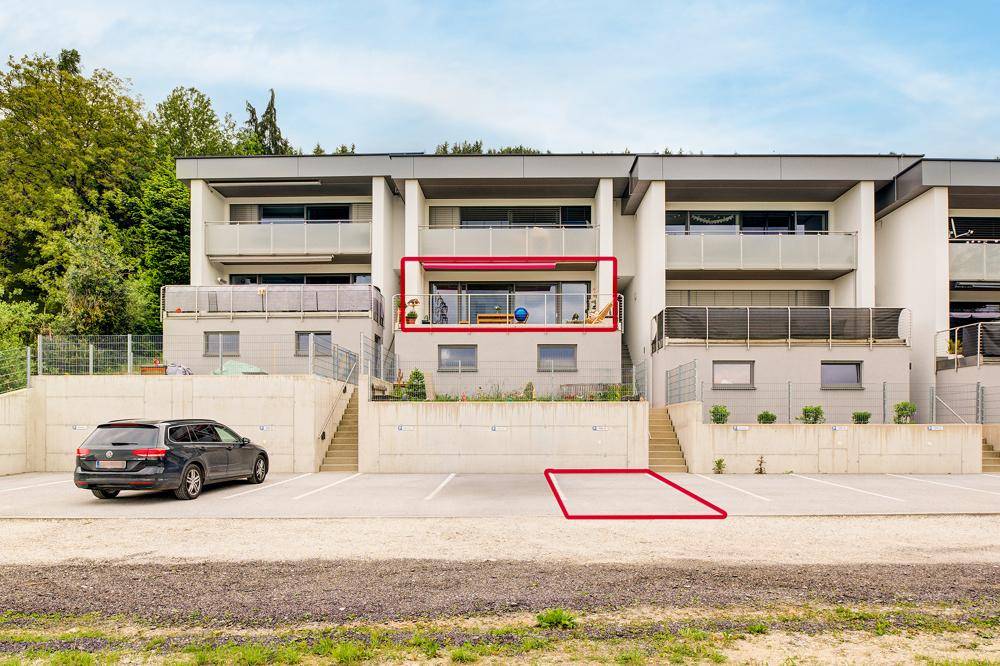Moderne Wohnanlage mit Balkonen und Außenparkplätzen, umgeben von grüner Landschaft.
