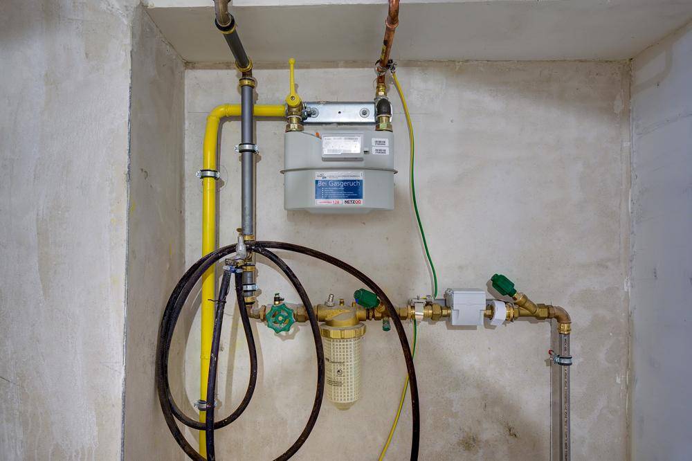 Gaszähler und Rohrleitungen in einem Technikraum mit Betonwänden.