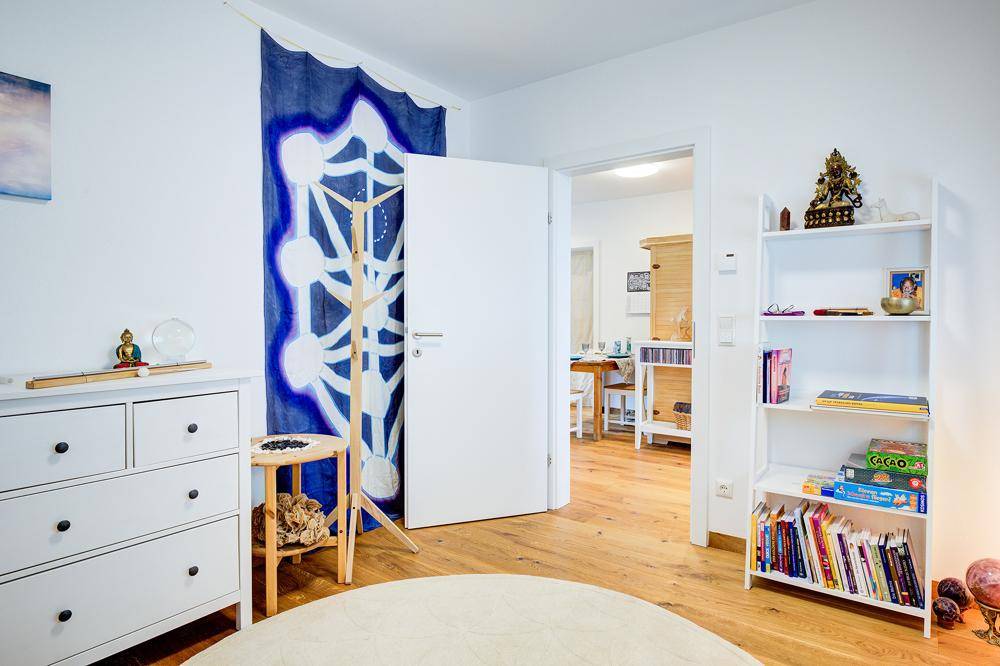 Helles Zimmer mit Holzboden und einem Bücherregal, das zu einem weiteren Wohnbereich führt.