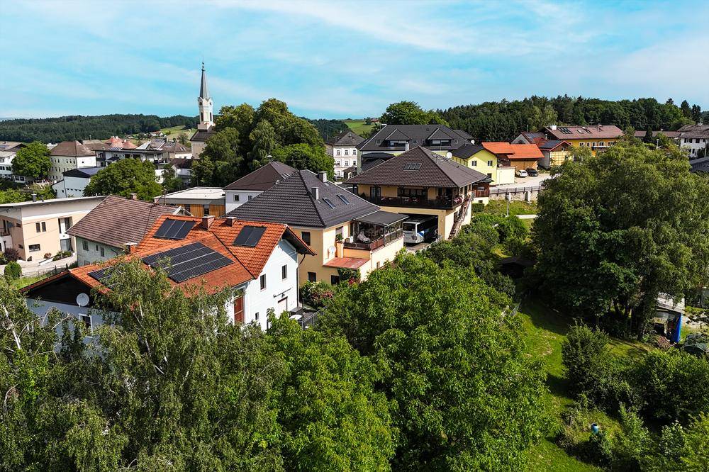 Panoramablick auf ein malerisches Dorf mit Kirche, umgeben von grünen Bäumen und Hügeln.