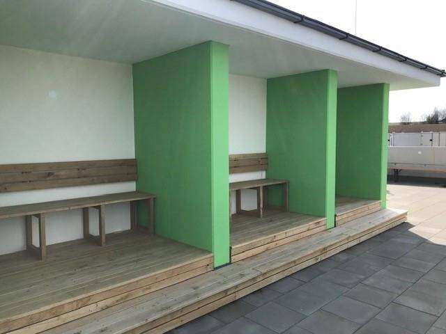 Überdachter Außenbereich mit Holzbänken und grünen Trennwänden, ideal zum Entspannen.