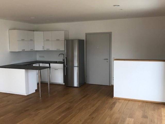 Offene Küche mit weißen Schränken, Edelstahlkühlschrank und hellem Holzfußboden.