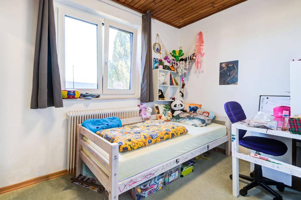 Helles Kinderzimmer mit Teppichboden, Fenster und Schreibtisch.