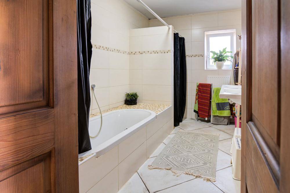 Badezimmer mit Badewanne, Duschvorhang und Fenster, gefliest in hellen Farben.