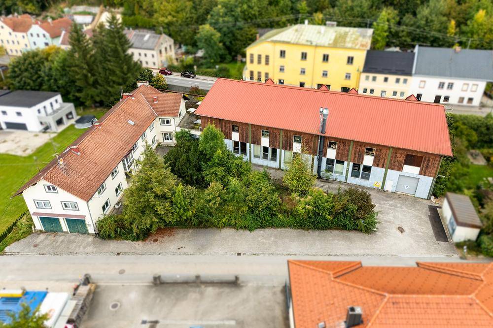 Übersicht aus der Vogelperspektive zeigt das Anwesen mit seinen Gebäuden, umgeben von Bäumen und einer gepflasterten Fläche.