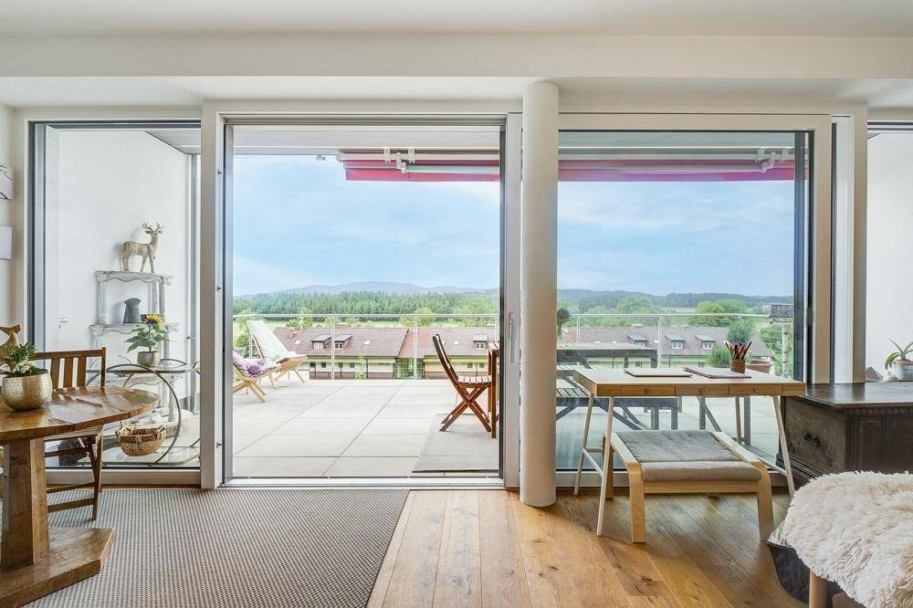 Heller Wohnbereich mit Holzboden und großen Schiebetüren, die zu einer geräumigen Terrasse führen.