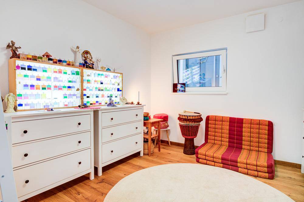 Freundliches Zimmer mit Holzboden, weißen Kommoden und einem Fenster für natürliches Licht.