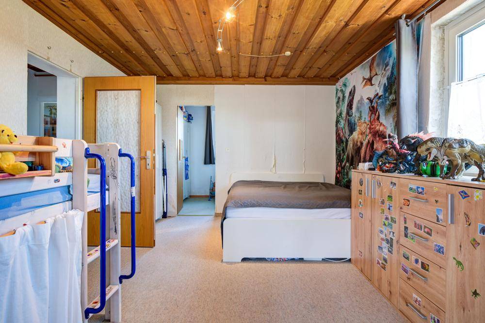 Kinderzimmer mit Holzbalkendecke, Teppichboden und bunten Wanddekorationen.