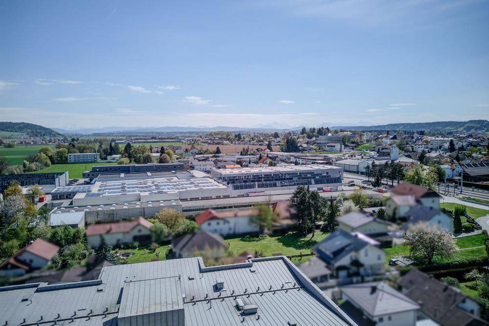 Luftaufnahme der Stadt mit Industriegebiet, Wohnsiedlungen und Bergen im Hintergrund.