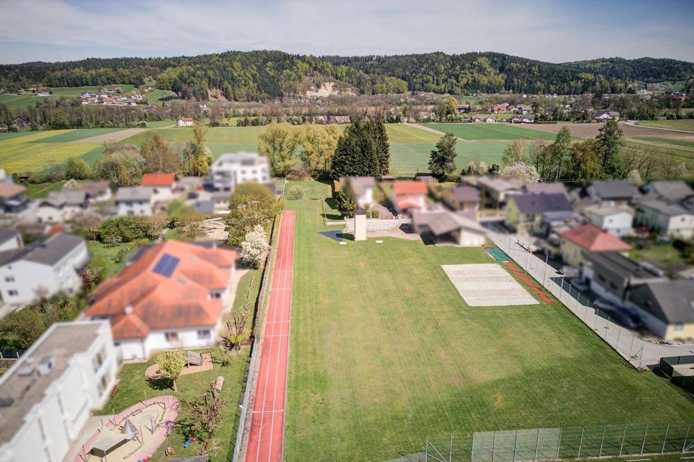 Weitläufige Grünfläche neben dem Haus mit Laufbahn und Blick auf die ländliche Umgebung.