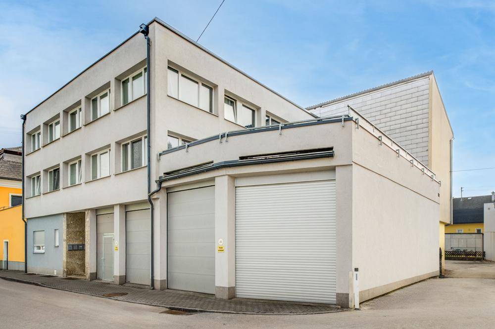Ansicht des Gebäudes von der Straße mit mehreren Garagentoren und Fenstern in den oberen Stockwerken.