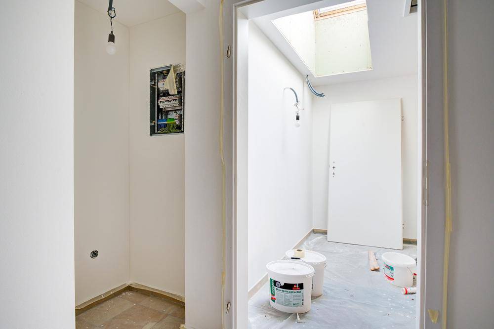 Flur im Rohbau mit Dachfenster, Elektroverteiler und Farbeimern auf dem Boden.