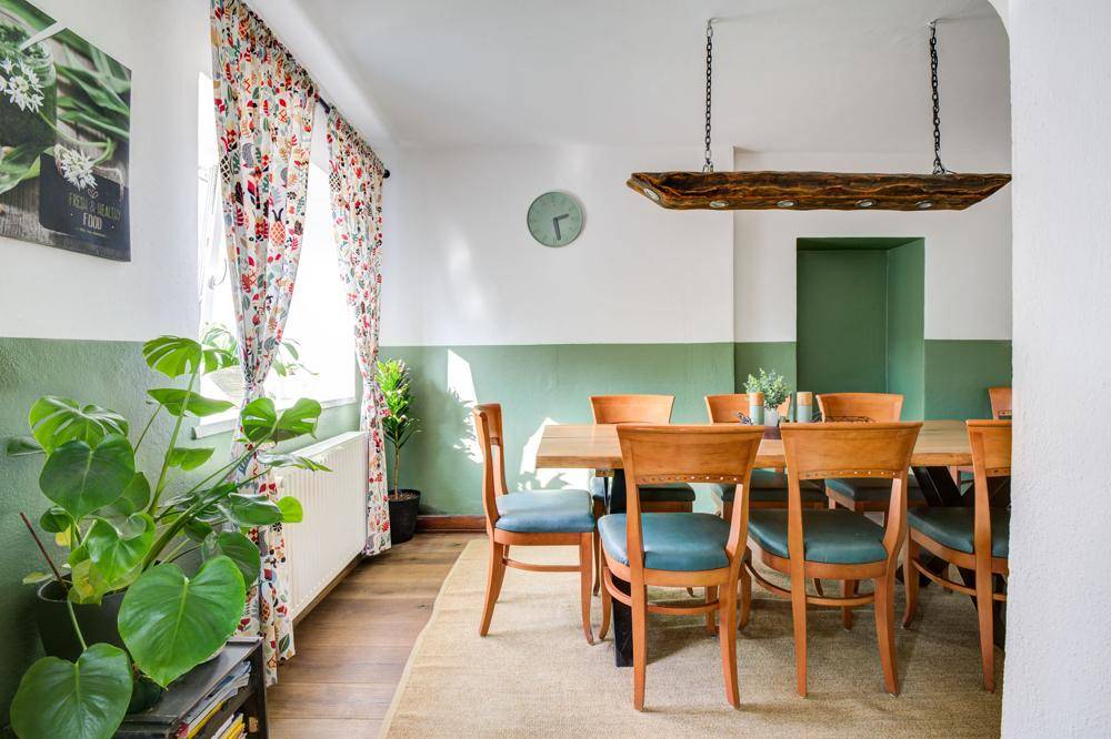 Heller Essbereich mit Holztisch, Stühlen und grünen Wänden, dekoriert mit Pflanzen.