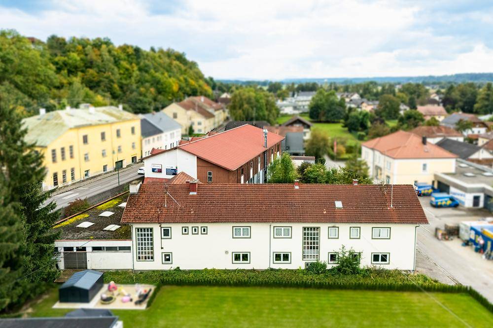 Panoramablick auf das Hauptgebäude mit angrenzendem Gartenbereich und Spielplatz, umgeben von einer grünen Hügellandschaft.