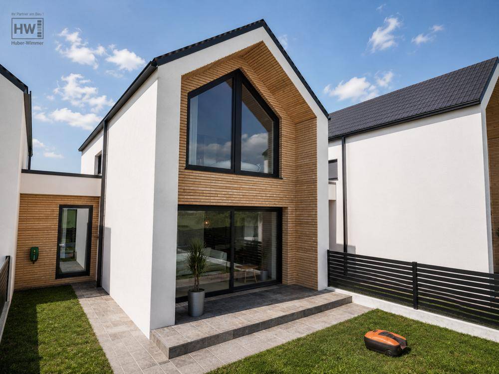 Gartenbereich eines modernen Hauses mit gepflegtem Rasen, Terrasse und Mähroboter.
