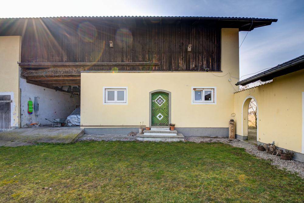 Seitenansicht des Hauses mit grünem Eingangstor und offenem Unterstand, umgeben von Rasen.