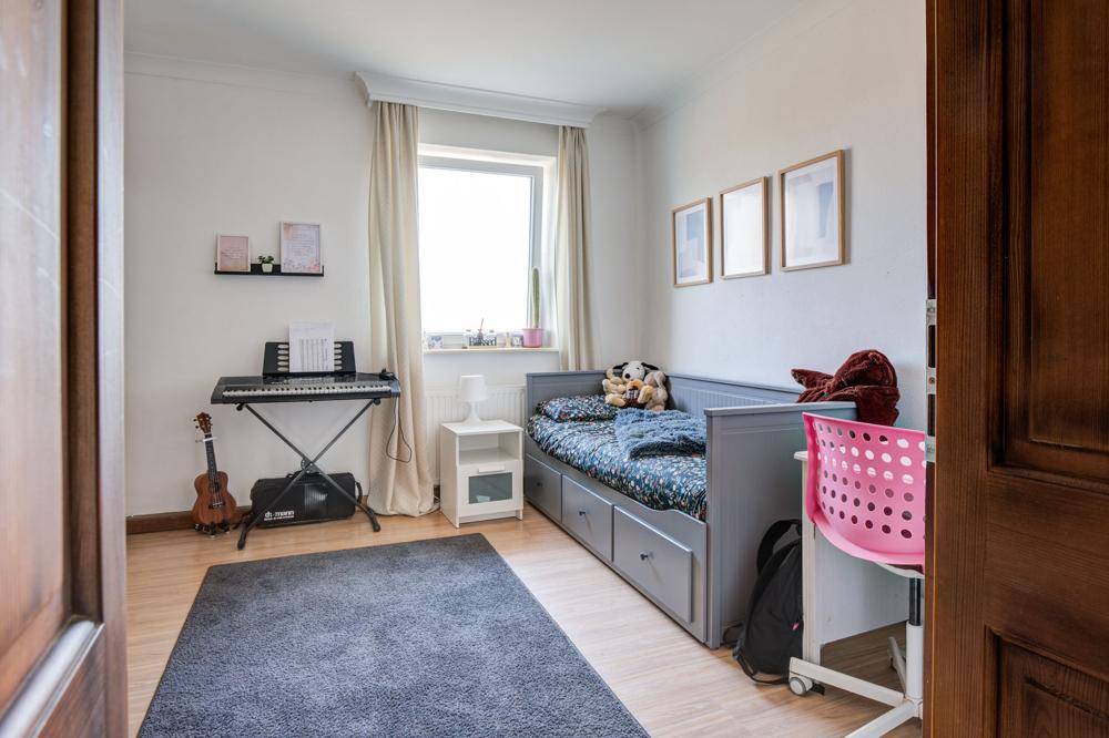 Kinderzimmer mit Einzelbett, Schreibtisch und Musikinstrumenten, hell durch großes Fenster.