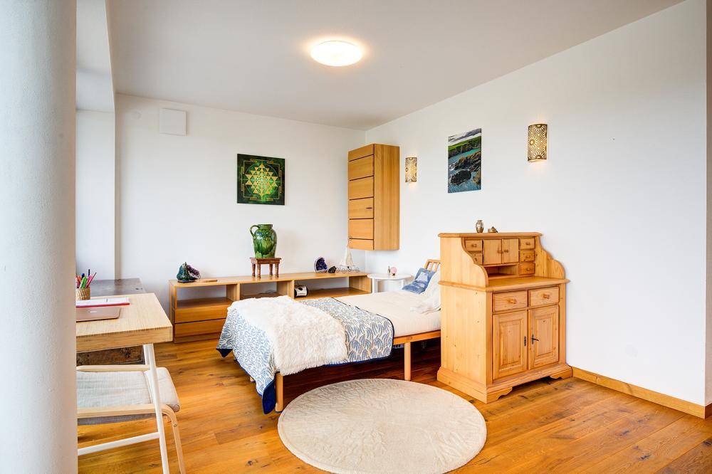 Helles Schlafzimmer mit Holzboden, einem Einzelbett und einem Schreibtisch in modernem Design.
