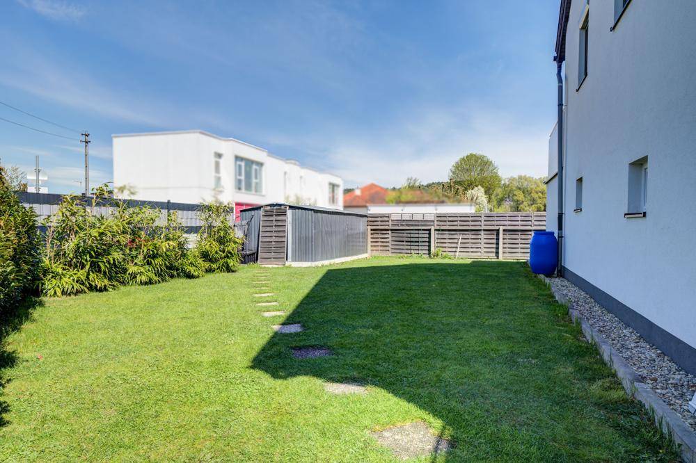 Gepflegter Gartenbereich mit Rasenfläche, Hecke und Gartenhaus im Hintergrund.